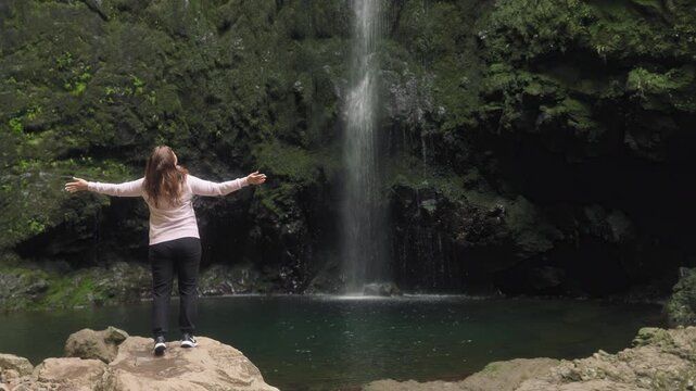 Woman with arms stretched in front of the main waterfall at Levada do Caldeirao Verde trail, Madeira island, Portugal