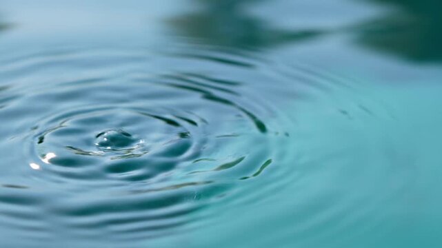 Slow motion close-up of water drop falling into calm pond with concentric ripples. Empty blurred turquoise water surface on the right for typography. 8k daylight. Pure nature serenity concept.