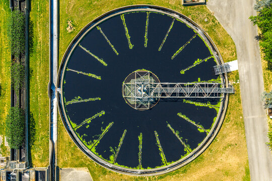 Aerial view of a circular water treatment tank with a rotating bridge and green algae patterns in Prato, Tuscany, Italy.