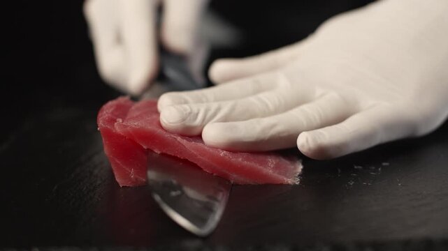 Professional chef slicing fresh raw tuna fillet with a sharp knife on a black board for sushi and sashimi in a japanese restaurant, close-up food preparation process