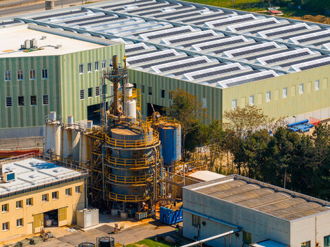 Aerial view of industrial factory buildings with solar panels on rooftops and complex machinery towers in Prato, Tuscany, Italy.