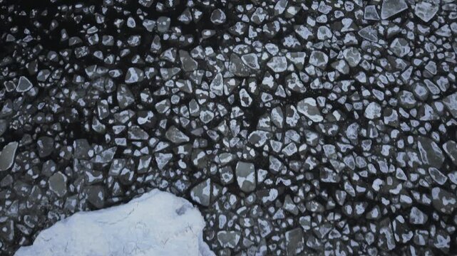Aerial view of the dark, frozen Baltic sea scattered with ice floes of varying sizes, creating a stark contrast of textures and tones, Mikoszewo, pomorskie, Poland.