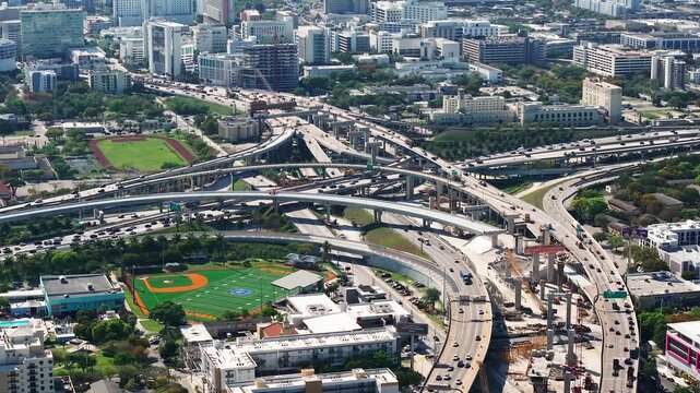 Aerial view of a complex highway interchange weaving through the urban sprawl, contrasting concrete with verdant green spaces, Miami, Florida, United States.