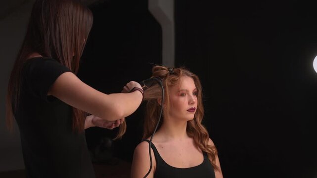 Hairdresser curling a young woman's long hair with a curling iron in a beauty salon. Professional hair styling process creating elegant waves for a glamorous makeover