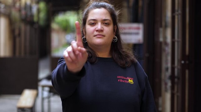 A brunette young woman clearly expresses disagreement by moving her finger to say no. Strong and direct gesture showing refusal and disapproval toward the camera.
