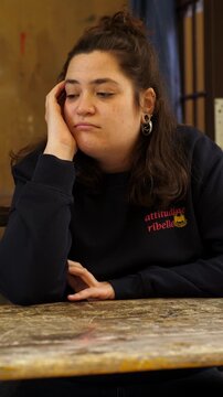 Vertical: Brunette woman rests her head on her hand, appearing bored and sad. Her low energy expression conveys fatigue, disinterest, and emotional heaviness in a quiet, intimate moment.