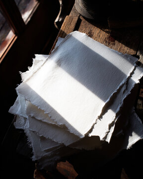 Stack of white handmade paper on rustic wood with dramatic light