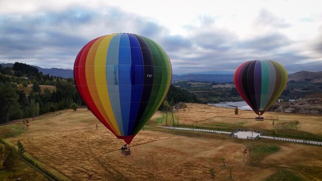 Queenstown, New Zealand - 13 April 2026: Aerial view of vibrant hot air balloons rising above the golden fields near Littles Road, contrasting with the distant mountains.