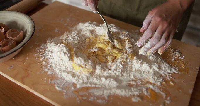 Woman preparing dough with flour and eggs for homemade pasta indoor - Italian food, culture and lifestyle concept