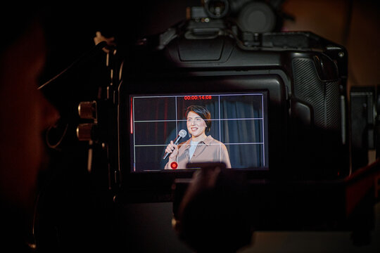 Close up of camera screen showing biracial middle aged woman speaking into microphone on stage during standup performance. Useful for live event promotion, media production, entertainment marketing
