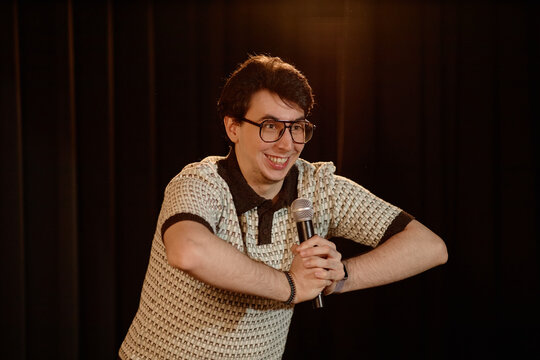 Portrait of young adult Caucasian man performing standup comedy on stage, holding microphone and engaging audience. Useful for entertainment marketing, live event promotion, comedy ads
