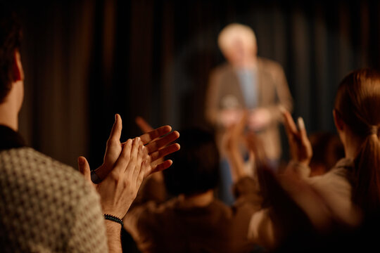 Audience applauding senior speaker during standup performance on stage, signaling live entertainment success. Useful for event promotion, comedy marketing, ticket sales campaigns

