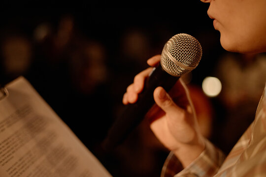 Close up of young adult speaker holding microphone and reading notes during standup performance on stage. Useful for comedy event promotion, live entertainment marketing, public speaking
