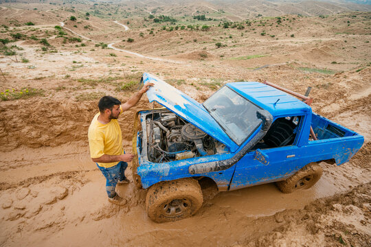 Man checking broken engine of off-road vehicle stuck in mud
