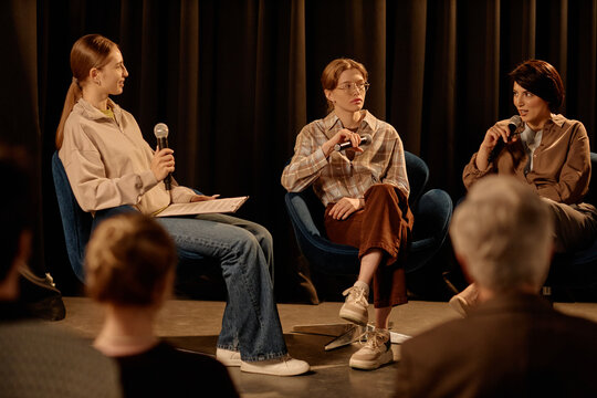 Young adult women speaking on stage during standup style panel discussion, holding microphones before audience. Useful for event promotion, public speaking, live talk marketing
