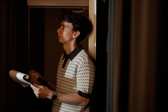 Young adult Caucasian man holding microphone and notes while preparing backstage for standup performance. Useful for comedy promotion, live event marketing, entertainment branding
