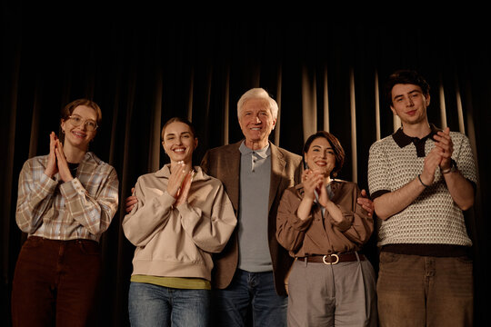 Portrait of multiethnic team standing on stage, clapping after standup performance and looking at camera. Useful for comedy promotion, event marketing, teamwork or audience engagement

