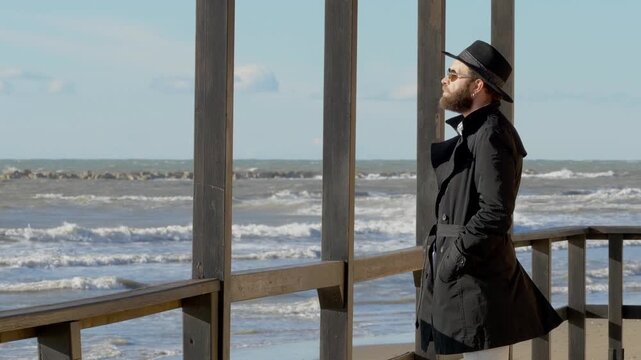 Young man with hat looking at the sea thinking about upcoming summer. Calm outdoor scene expressing hope, reflection and anticipation of future moments.