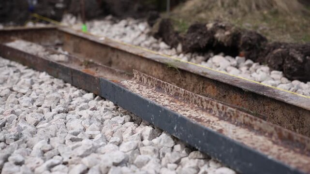 Two parallel rusted rails rest on crushed stone ballast as a taut yellow guideline runs along the outer rail. Shallow depth of field, muted tones, overcast daytime.