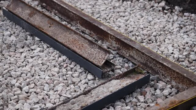 Close up captures rusted rail segments and short beams on pale ballast. Shallow depth of field isolates midplane details, with moss, flaking, and a yellow guideline.