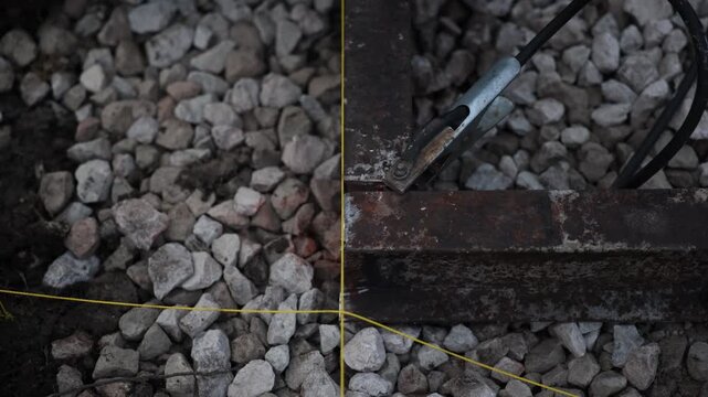 Rusty steel rail is clamped with a grounding clip as an oxy fuel torch forms a molten tip and faint orange glow, with yellow guide strings and brief sparks near the joint.