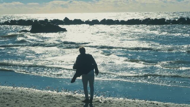 Young man picking up a stone and throwing it into the sea in anger. Outdoor scene showing frustration, tension and emotional outburst by the ocean.