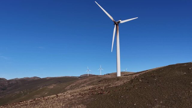 Aerial view of several wind turbines standing tall on the peaks of lush mountains under a clear blue sky, Amarante, Portugal.