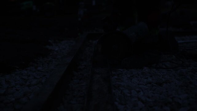 Worker operates angle grinder on rail track at night, sparks form bright orange streaks across ballast, red gloves steady tool, high shutter speed freezes motion