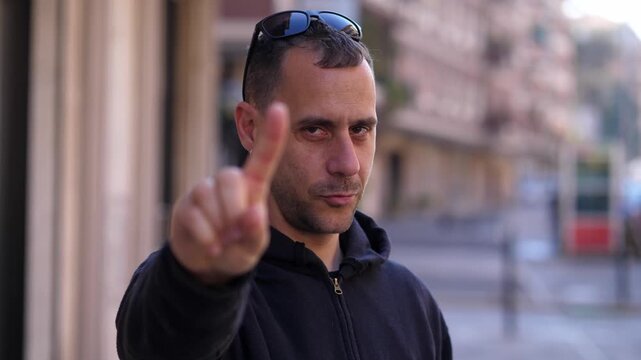 Young man in a black hoodie makes a clear no gesture with his finger, expressing disagreement. The scene highlights refusal and strong opinion.