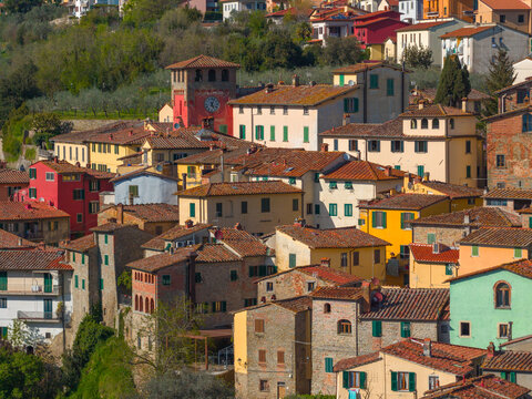 Aerial view of historic stone houses with terracotta roofs and a prominent red clock tower in Loro Ciuffenna, Tuscany, Italy.