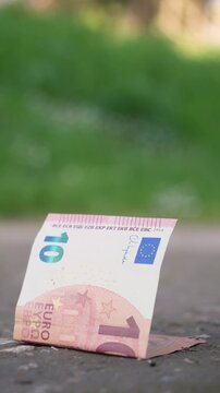 Vertical: Ten euro banknote rests on the ground waiting to be found. The scene suggests opportunity, chance, and unnoticed value in a simple everyday setting.