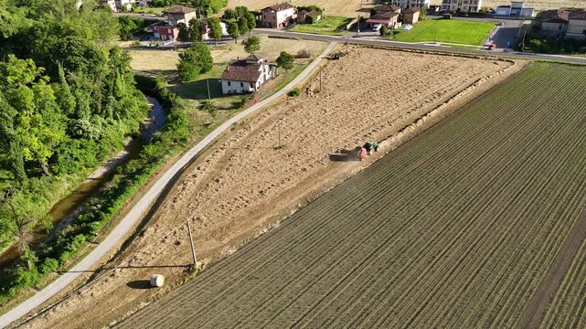 Harvested field with tractor forming hay bales near Castello di Castelnuovo Fogliani in Castelnuovo Fogliani, Emilia-Romagna, Italy