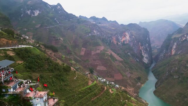 Aerial drone footage of a cliffside cafe overlooking Tu San Canyon and the Nho Que River with terraced hills and a winding mountain road in northern Vietnam.