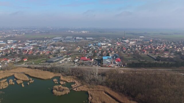 Sz&eacute;kesfeh&eacute;rv&aacute;r, Hungary, industrial suburb and S&oacute;st&oacute; Salt Lake with warehouses, factories, gokart track, wetlands, and surrounding fields captured in a wide aerial panorama under a cloudy sky.
