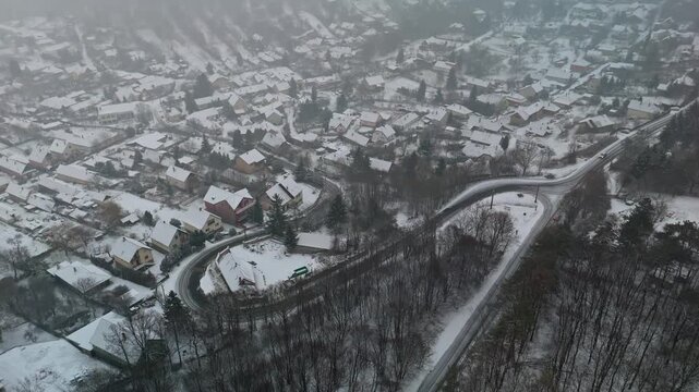 Pilisszentl&aacute;szl&oacute;, a traditional mountain village in Hungary's Pilis Mountains, is seen from above with snow-covered houses, winding roads, and surrounding frosted woodland during winter.