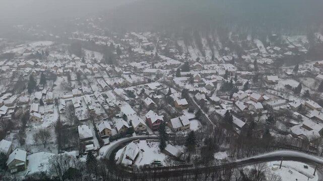 Pilisszentl&aacute;szl&oacute;, remote mountain village in Hungary's Pilis Mountains is seen covered in fresh snow with traditional houses, frosted trees and winding roads in a tranquil winter landscape from above.
