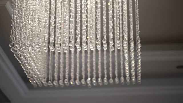 Extreme close-up of crystal bead strands on a large chandelier, showing transparent droplets and vertical rows against a neutral beige ceiling