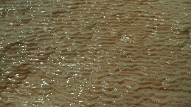 Extreme close up of limestone travertine formations with a thin layer of transparent water trickling over textured patterns, highlighting natural detail and geology.