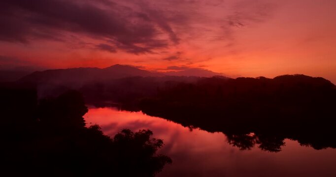 Vibrant red and orange sunset reflecting on a river surrounded by jungle silhouettes near Tayrona Park, Colombia. Aerial forward, copy space