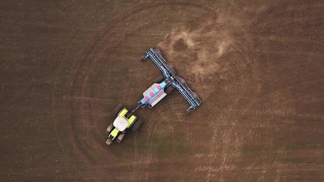 Aerial perspective of a tractor with a cultivator tilling brown soil in a field, showing distinct furrows and agricultural activity in the landscape