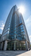 Fototapeta premium Towering glass skyscraper reaches toward a clear blue sky with a bright sunburst at its peak. Modern ambition and business success. Ideal for real estate or corporate marketing.