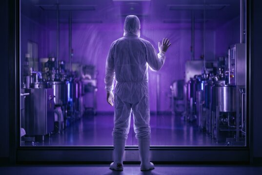 Man in protective suit hand on glass window industrial factory interior