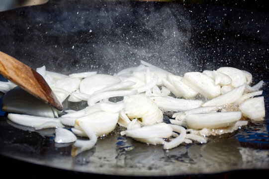 Close-up of sliced onions frying in hot oil on a disc plough pan. Traditional outdoor cooking dynamic splatter.