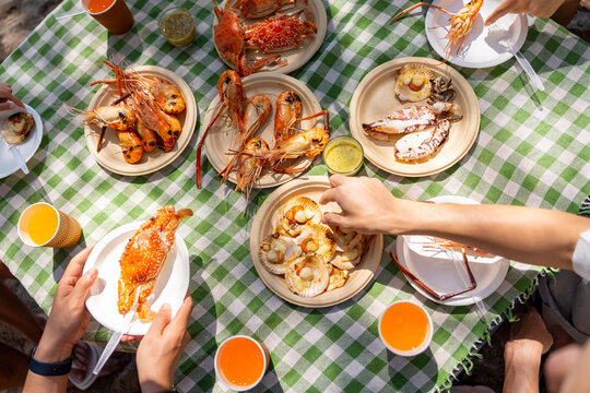 Top view Group of Asian friends sharing seafood meal together at outdoor picnic table, people enjoying summer beach holiday vacation active lifestyle social gathering party concept