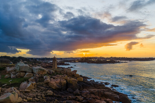 Aerial view of Mean Ruz Lighthouse at Ploumanac'h on the Pink Granite Coast with dramatic sunset clouds and rocky shoreline Perros-Guirec, Brittany, France.
