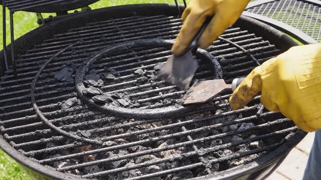Person wearing yellow gloves cleans charcoal grill grates with spatula, showing progression of cleaning actions in outdoor setting
