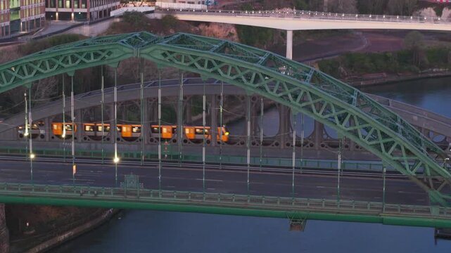 Aerial telephoto shot of a Tyne and Wear Metro train crossing the Monkwearmouth Railway Bridge at dawn, with the Wearmouth Bridge in the foreground.