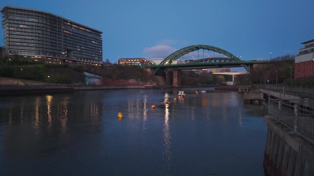 Low-altitude aerial drone shot flying over the River Wear in Sunderland at dawn, featuring the illuminated Wearmouth Bridge and city skyline in the background.