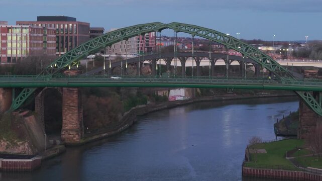 Telephoto drone clip tracking around the Wearmouth Bridge and over River Wear in Sunderland at dawn. City lights are still on 
