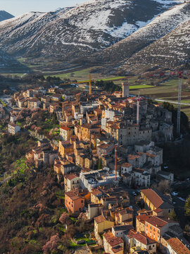 Aerial view of the medieval stone village with terracotta roofs nestled against snow-capped mountains in Santo Stefano di Sessanio, Abruzzo, Italy.